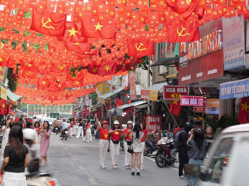Bustling street lined with overhead flags in Hanoi National Day Celebrations atmosphere.