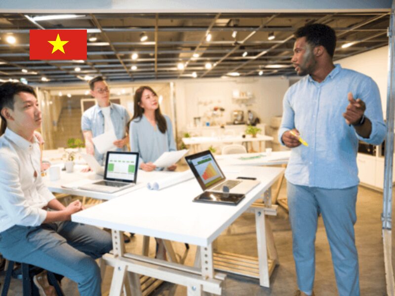 Diverse Foreign Workers in Vietnam collaborating in a modern office with Vietnam flag, discussing investment strategies.