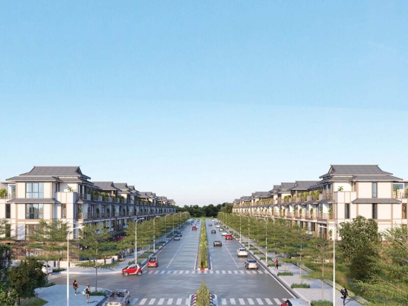 Aerial view of modern commercial housing development in HCMC featuring 74 pilot areas with traditional tiled roofs, tree-lined boulevards, and pedestrian pathways under a clear blue sky.