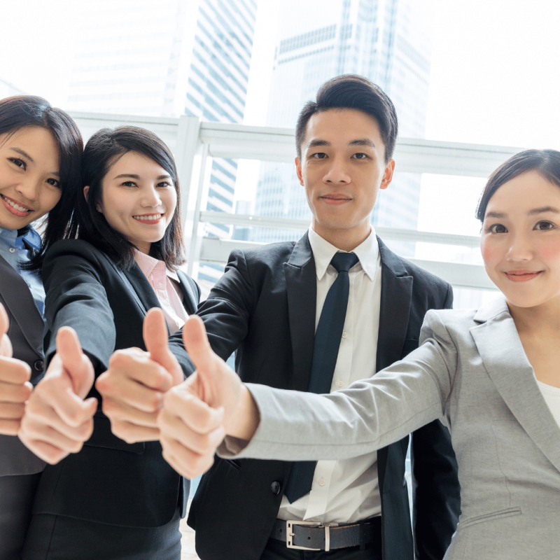 Diverse business team giving thumbs up in a modern office with city skyline for post-arrival support.